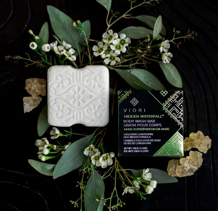 Viori Hidden Waterfall body wash bar with floral design, packaging, green leaves, and natural resin on dark background