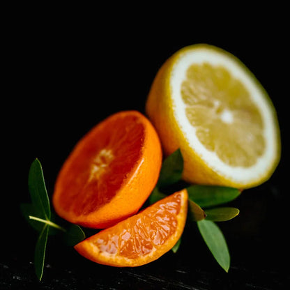 Close-up of fresh sliced citrus fruits including orange and lemon segments with green leaves on black background
