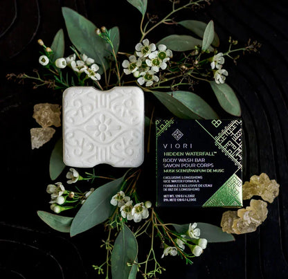 Viori Hidden Waterfall body wash bar with floral design, packaging, green leaves, and natural resin on dark background