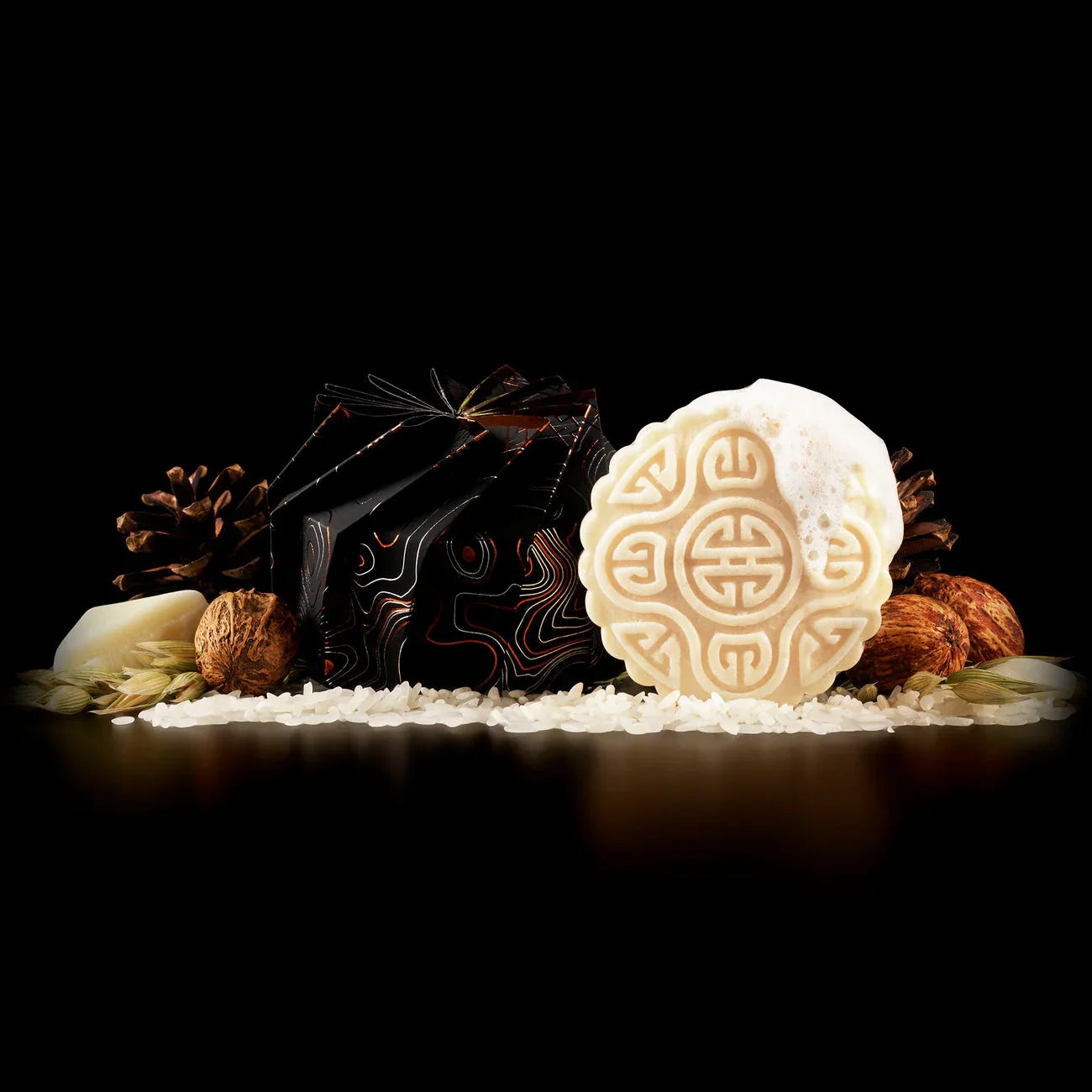 Decorative Native Essence shampoo bar with foam, surrounded by natural ingredients like rice, nuts, pine cones, and grains on black background