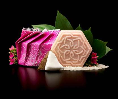 Hexagonal patterned soap bar with coconut, rice grains, green leaves, and magenta floral packaging on black surface