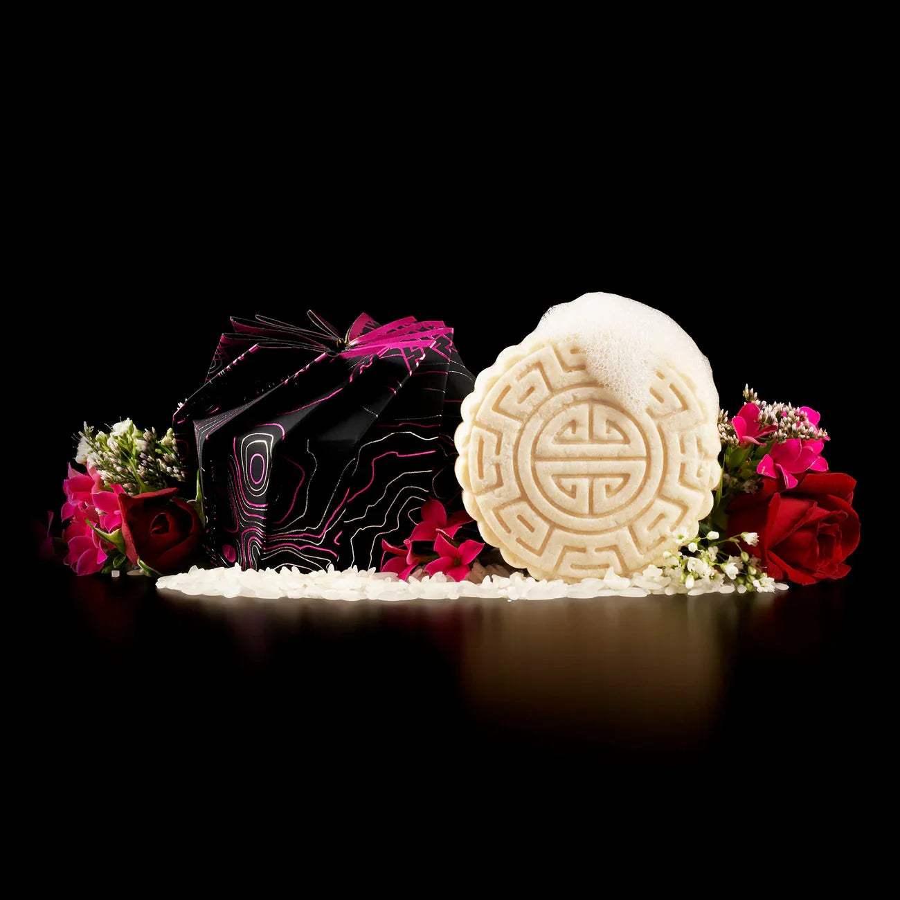 EPS bee hive-shaped shampoo bar with foam, surrounded by rice grains and vibrant flowers on black background