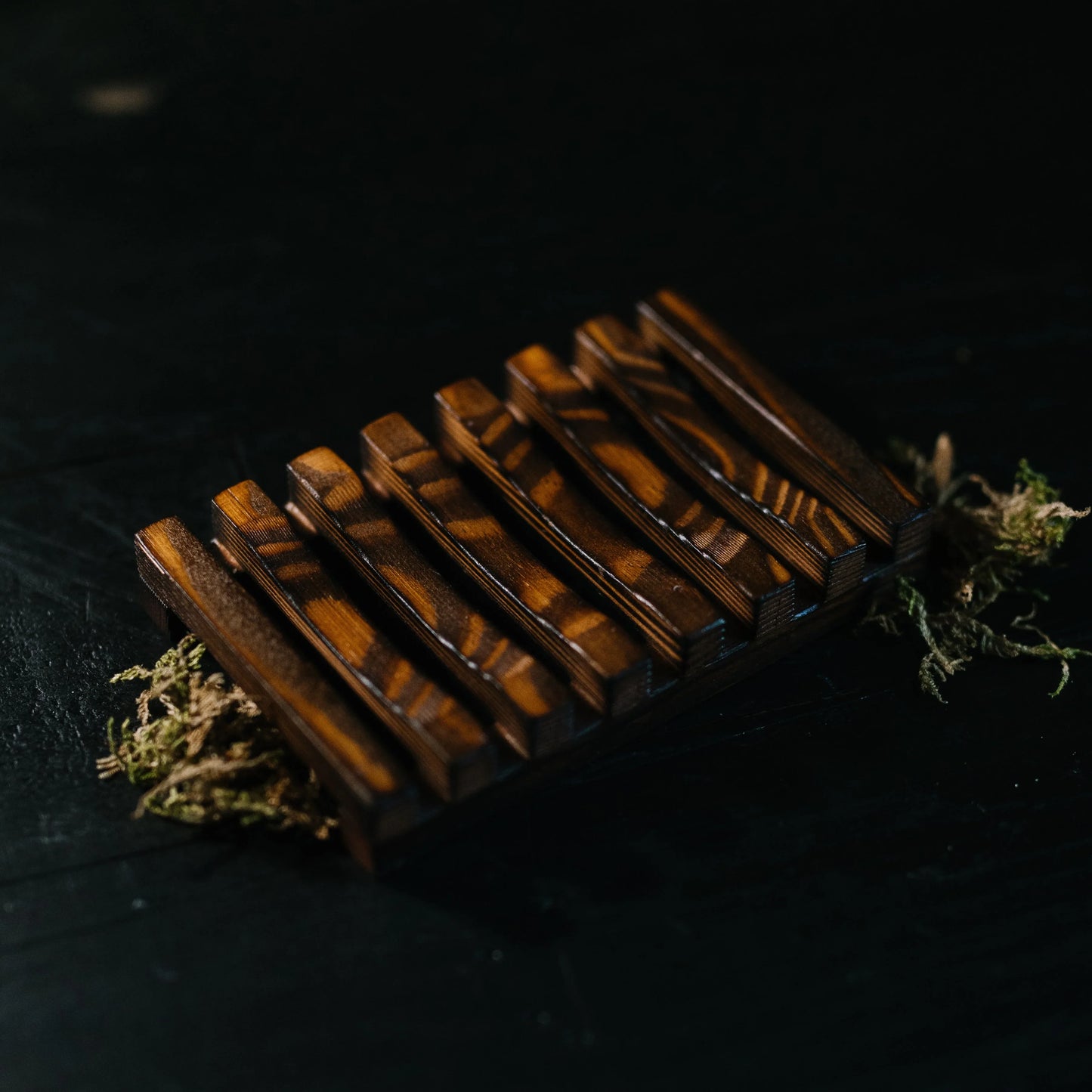 Close-up of a dark wood EPS bee hive frame with distinctive grain, placed on dark surface with moss