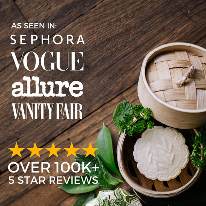 Tea tree shampoo bar with embossed leaf design in a bamboo container surrounded by fresh greenery on wooden surface